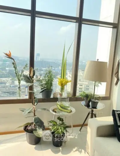 Bright living room with large windows and city view, featuring indoor plants and modern decor.