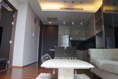 Modern living room with open kitchen, featuring sleek furniture and contemporary lighting.