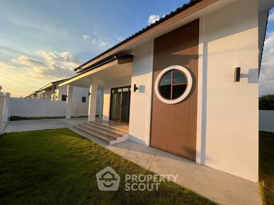 Modern single-story home with unique circular window and spacious lawn at sunset.