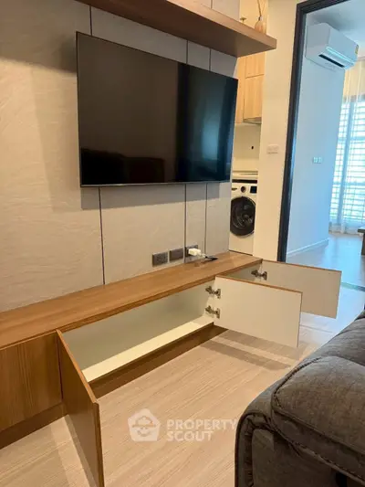 Modern living room with wall-mounted TV and sleek wooden storage unit, featuring a glimpse of a laundry area.