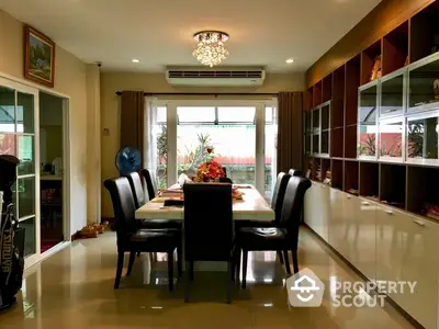 Elegant dining area with polished tile flooring, a modern chandelier, and large windows offering ample natural light and garden views, perfect for family gatherings.