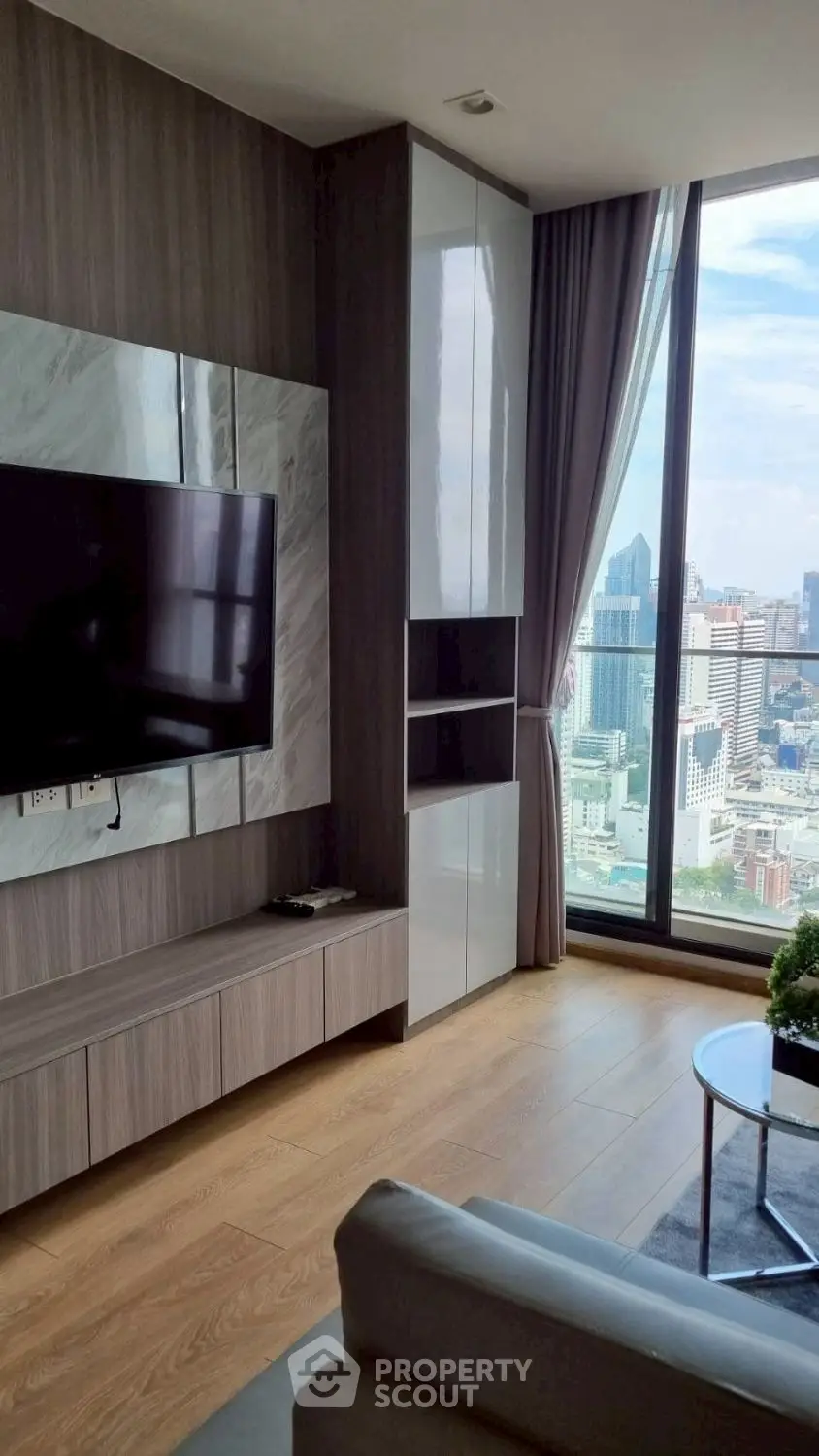 Modern living room with city view, featuring sleek TV setup and floor-to-ceiling windows.