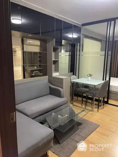 Elegantly furnished apartment interior with modern design, featuring a cozy living area with a plush sofa, glass coffee table, and a dining space visible through glass partitions, all under warm ambient lighting.