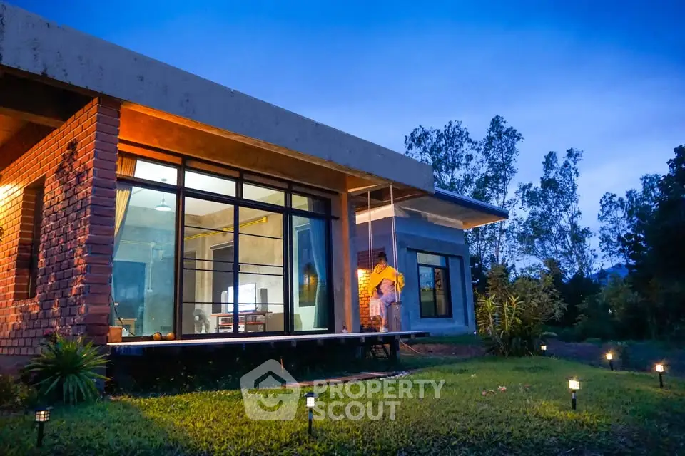 Modern brick house with large windows and lush garden at dusk