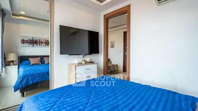 Modern bedroom with blue bedding, wall-mounted TV, and mirrored closet in stylish apartment.
