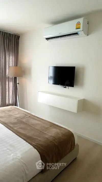 Modern bedroom with wall-mounted TV and air conditioning, featuring elegant decor and natural light.