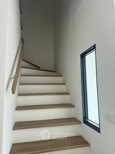 Modern staircase with wooden steps and sleek handrail in a bright interior space.