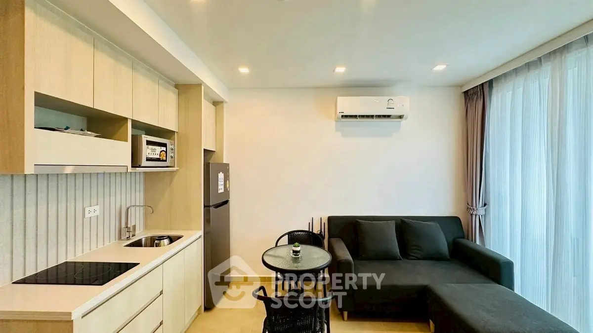 Modern open-layout living room with kitchenette, featuring sleek furniture and large windows for natural light.