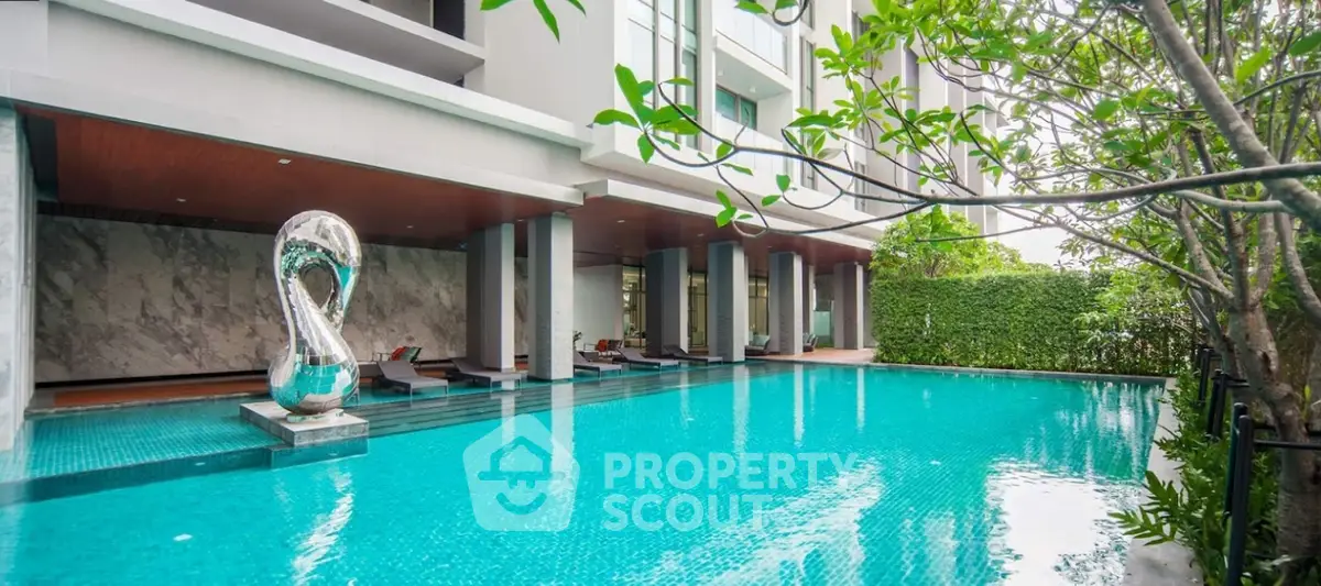 Luxurious condominium pool area with modern sculpture and lush greenery