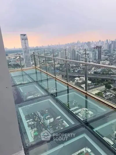 Stunning high-rise balcony with glass floor offering breathtaking cityscape views at sunset.