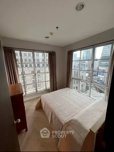 Bright corner bedroom with large windows offering city views in modern apartment.