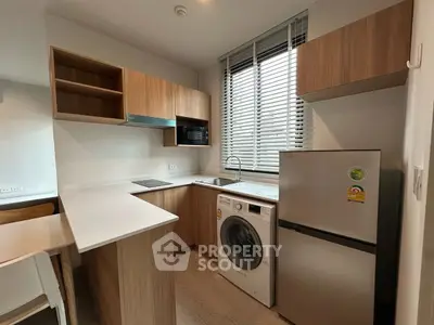 Modern kitchen with wooden cabinets, washing machine, and fridge under natural light.