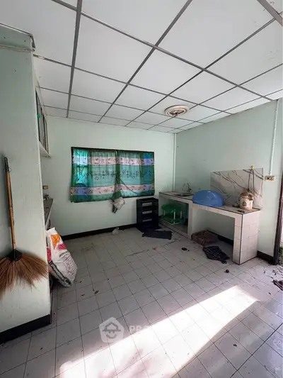 Spacious kitchen with tiled floor and natural light, ideal for renovation.