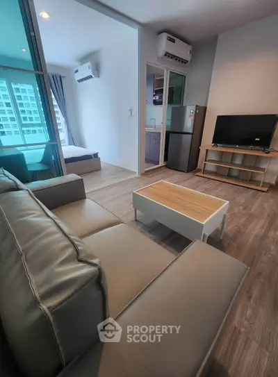Modern living room with sleek furniture and open view to bedroom and kitchen.