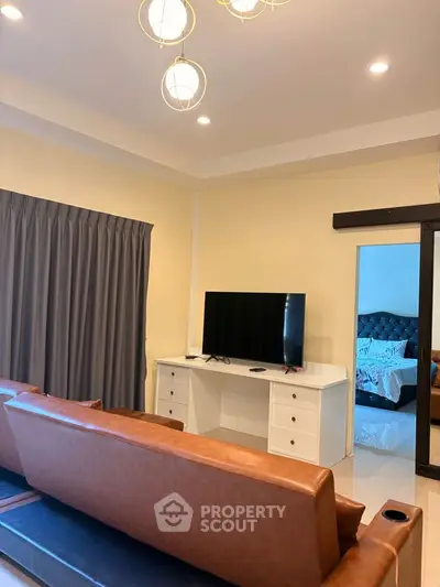 Modern living room with leather sofa and flat-screen TV, adjacent to a cozy bedroom.