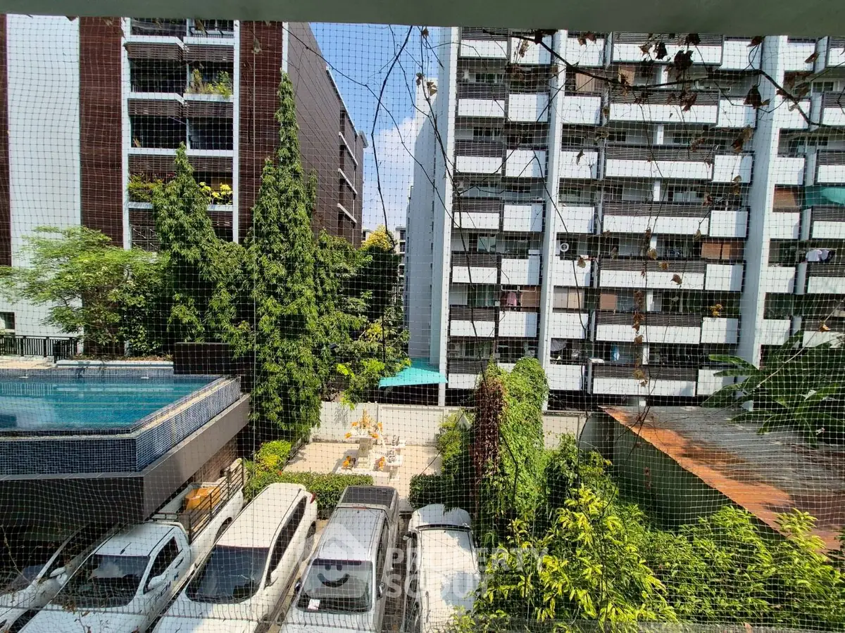 Urban apartment view with pool and parking area, surrounded by greenery and modern buildings.