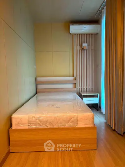 Modern bedroom with wooden flooring and air conditioning, featuring a minimalist bed and nightstand.