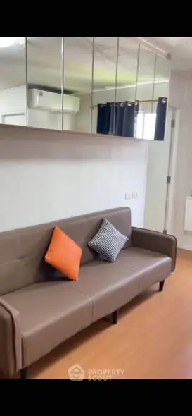 Modern living room with sleek brown sofa and mirrored wall for spacious feel.