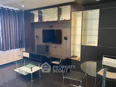 Modern living room with sleek black furniture and glass accents, featuring a wall-mounted TV and elegant decor.