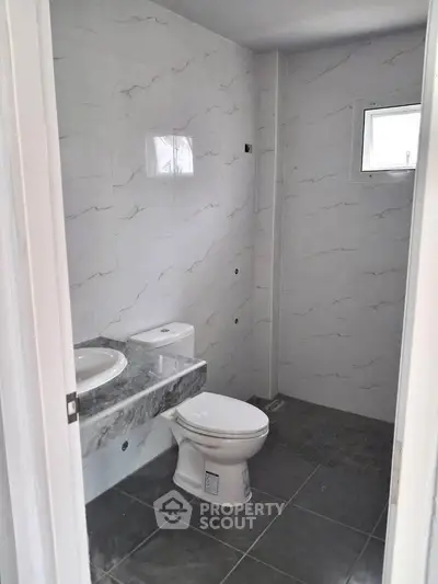 Modern bathroom with sleek marble tiles and compact design, featuring a stylish sink and toilet.