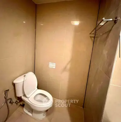 Modern bathroom with sleek beige tiles and a white toilet, offering a clean and minimalist design.