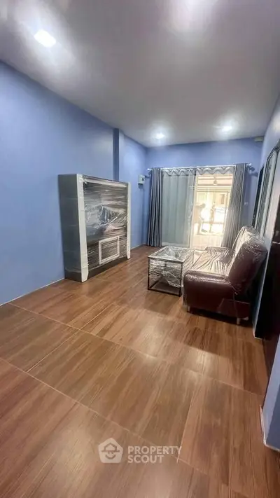Modern living room with blue walls, wooden flooring, and large window for natural light.
