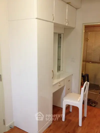 Compact bedroom with built-in wardrobe and vanity, featuring sleek white furniture and wooden flooring.