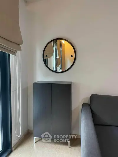 Modern living room with sleek cabinet and round mirror, featuring a cozy gray sofa and large window.