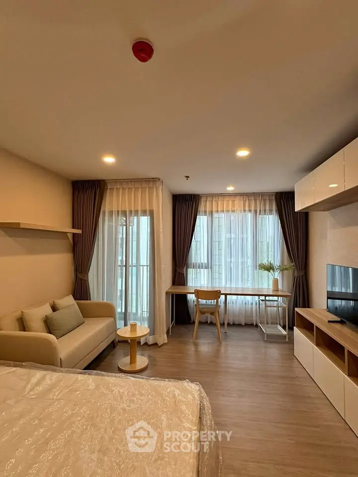 Modern studio apartment with cozy living area and large windows for natural light.