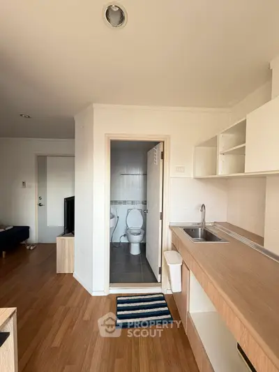 Compact studio apartment with open kitchen and bathroom view, featuring modern wooden flooring.