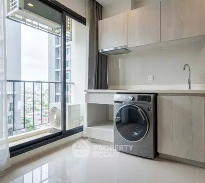 Modern laundry area with sleek washer and city view from large window in high-rise apartment.