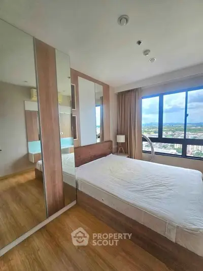 Modern bedroom with large window and mirrored wardrobe offering stunning city views.
