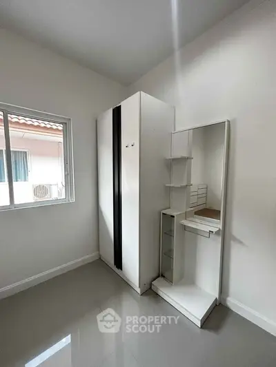 Minimalist bedroom with sleek white wardrobe and mirror, offering ample storage space and modern design.