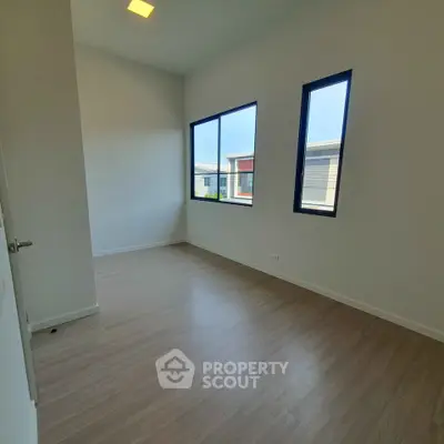 Bright and airy bedroom with large windows and wooden flooring in modern home.