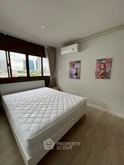Modern bedroom with large window and city view, featuring stylish wall art and air conditioning.