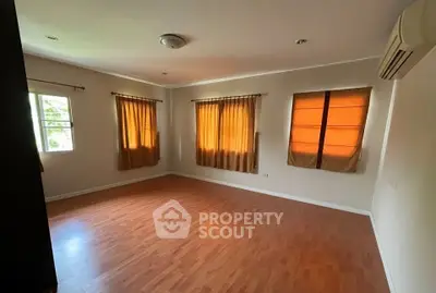 Spacious empty room with wooden flooring and large windows, perfect for customization.