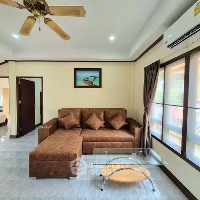Spacious living room with modern brown sofa and glass coffee table, featuring elegant ceiling fan and natural light.