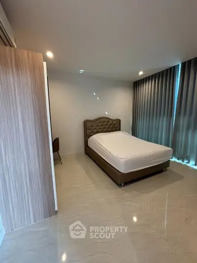 Spacious bedroom with modern decor and natural light, featuring a comfortable bed and elegant curtains.