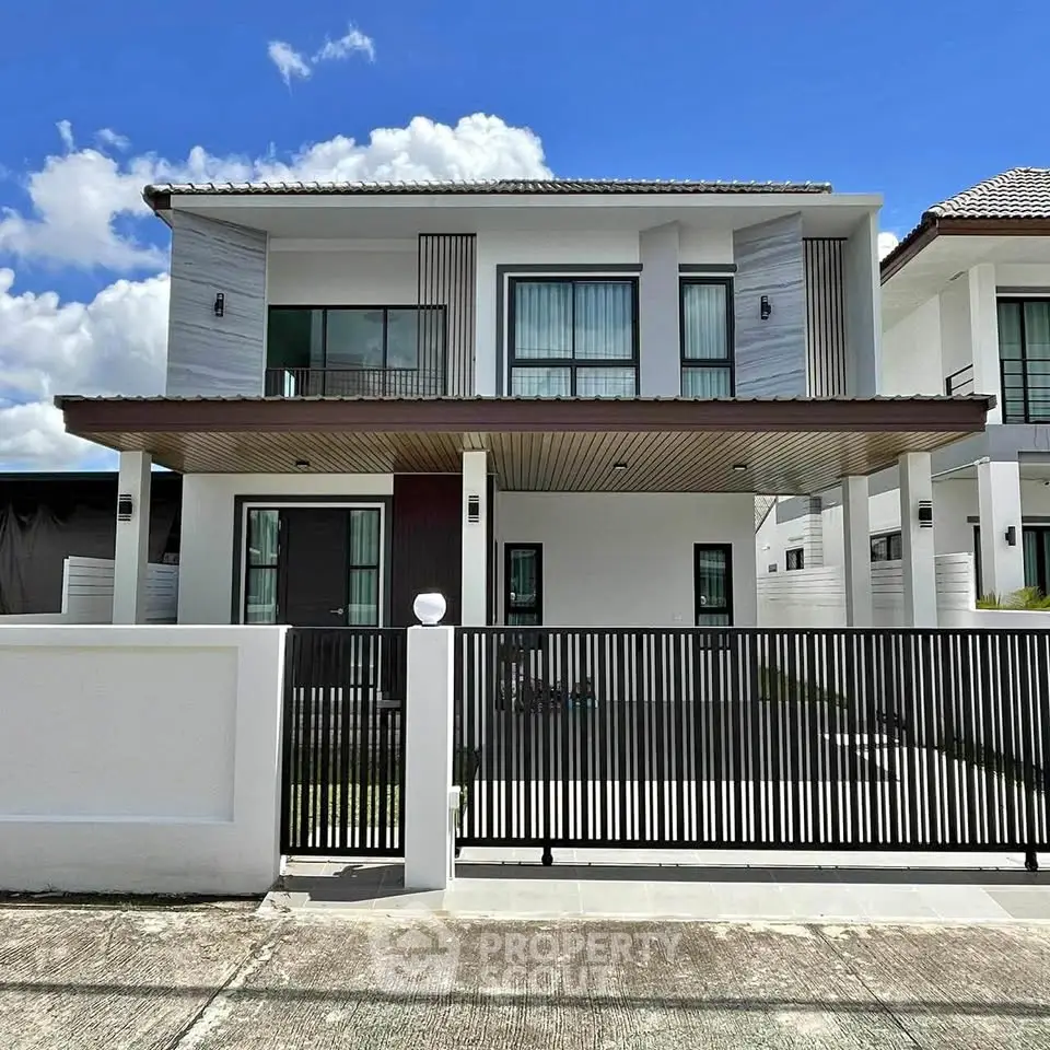 Modern two-story house with sleek design and gated entrance under clear blue sky.