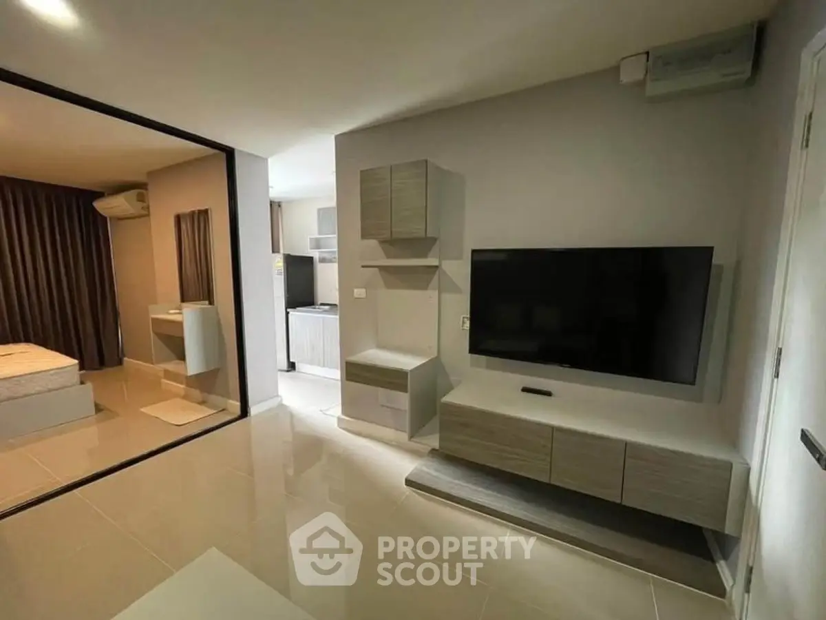 Modern living room with sleek TV unit and view into cozy bedroom
