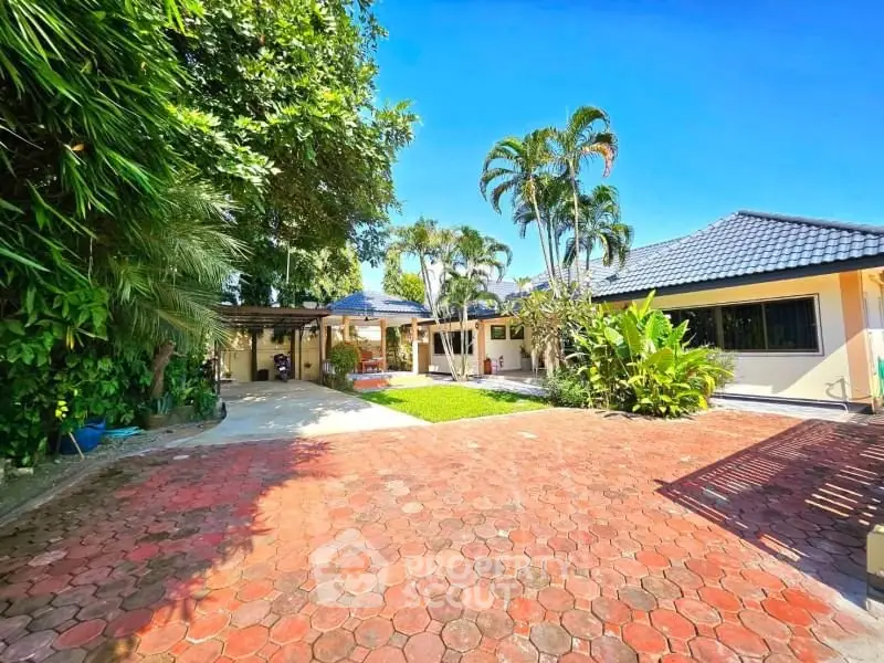 Spacious tropical villa with lush garden and paved driveway under clear blue sky.
