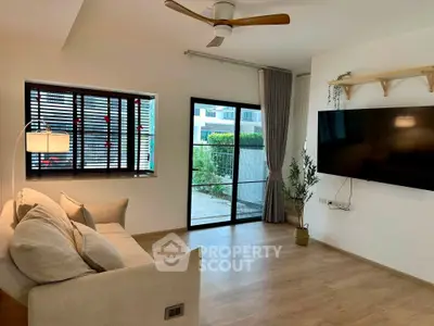 Modern living room with large TV, cozy sofa, and garden view through glass doors.