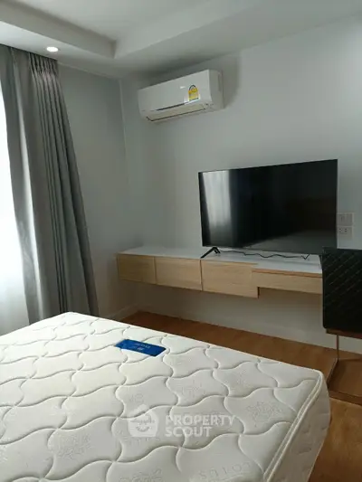 Modern bedroom with wall-mounted TV and air conditioning, featuring a stylish floating desk and comfortable mattress.