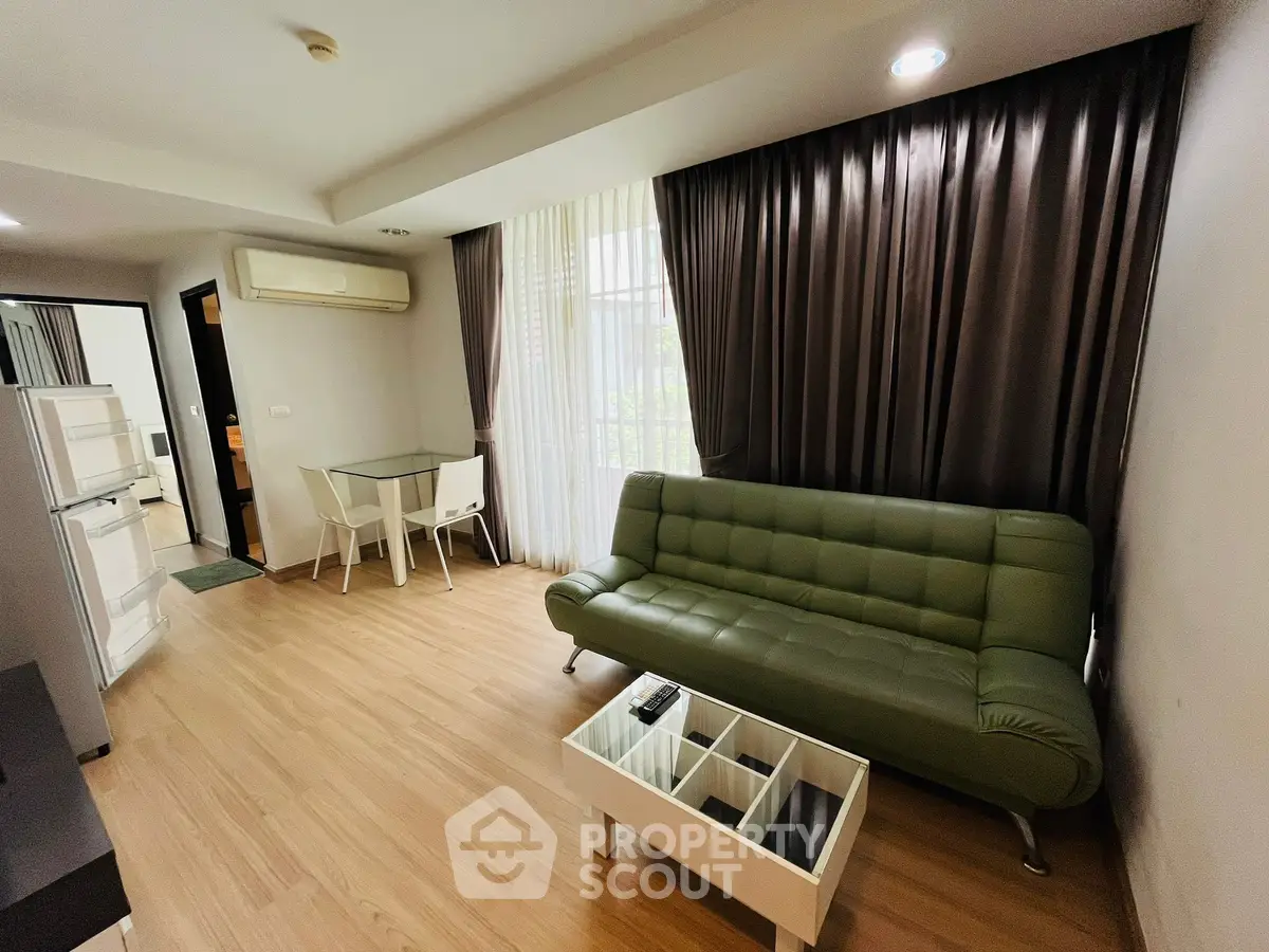 Modern living room with green sofa, dining area, and natural light through large windows.