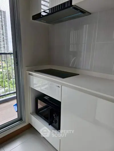 Modern kitchen with sleek appliances and balcony view in high-rise apartment.