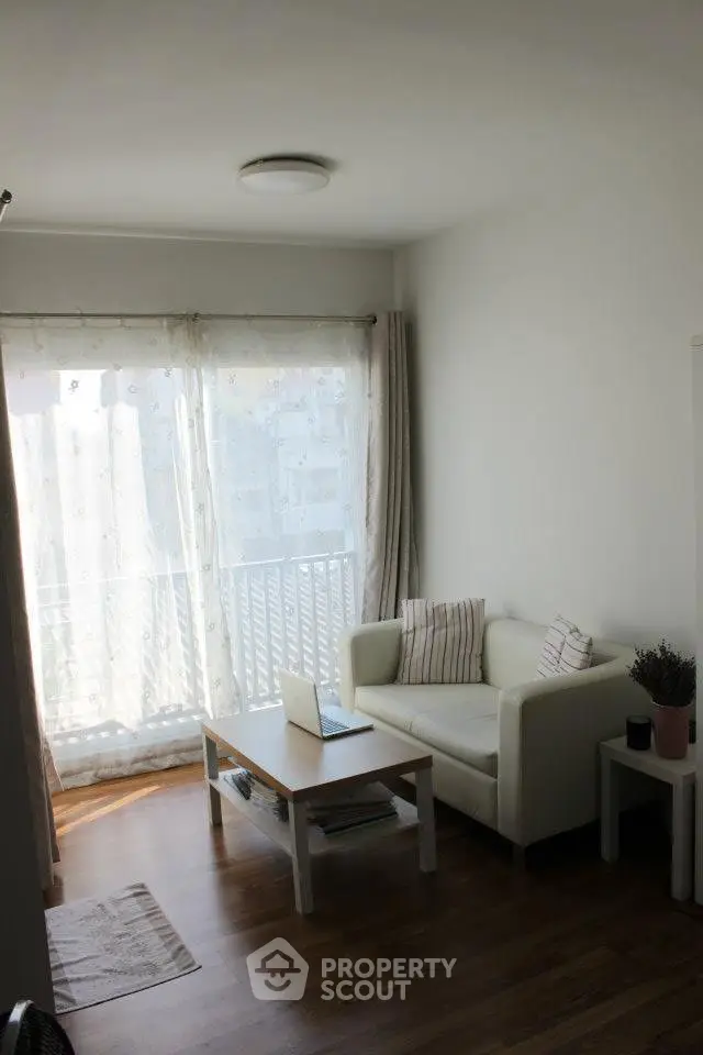 Cozy living room with natural light and balcony access, featuring a white sofa and wooden flooring.