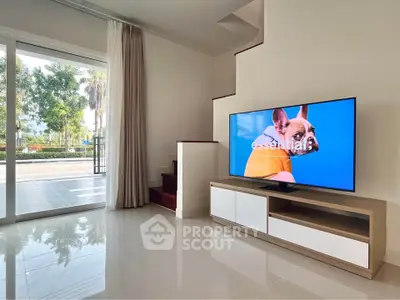Modern living room with sleek TV setup and large glass doors opening to a garden view.