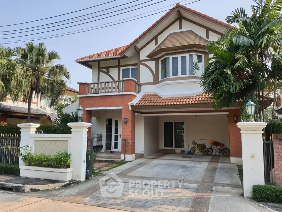 Charming two-story house with red brick facade and lush palm trees in a serene neighborhood.