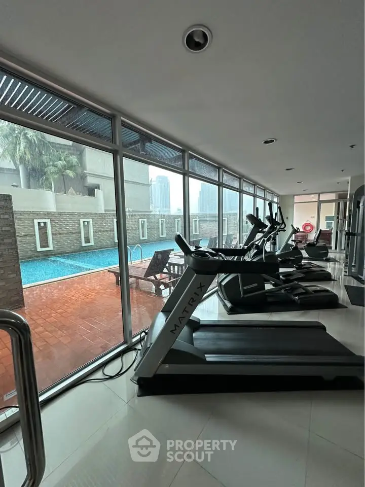 Luxurious gym with modern equipment and pool view in upscale residential building.