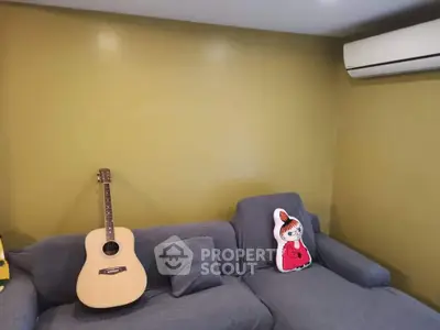Cozy living room with gray sofa, guitar, and air conditioning unit on mustard wall.